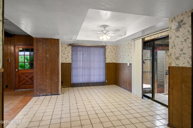 spare room featuring a raised ceiling, wood walls, and ceiling fan