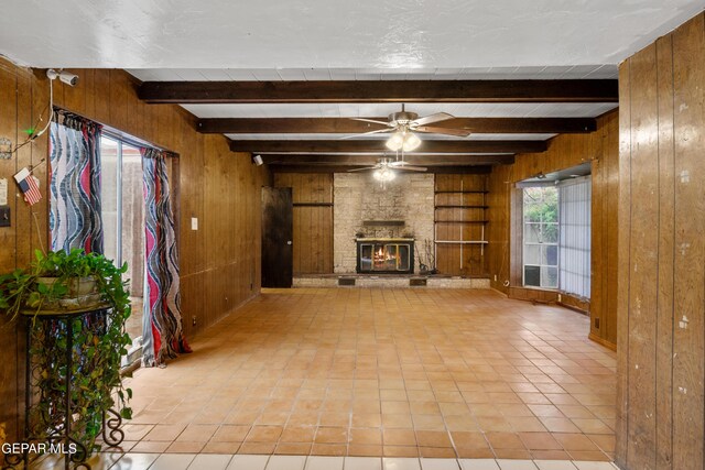 unfurnished living room featuring wood walls, beamed ceiling, a fireplace, tile patterned floors, and ceiling fan