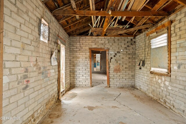 misc room with brick wall, vaulted ceiling, and concrete floors