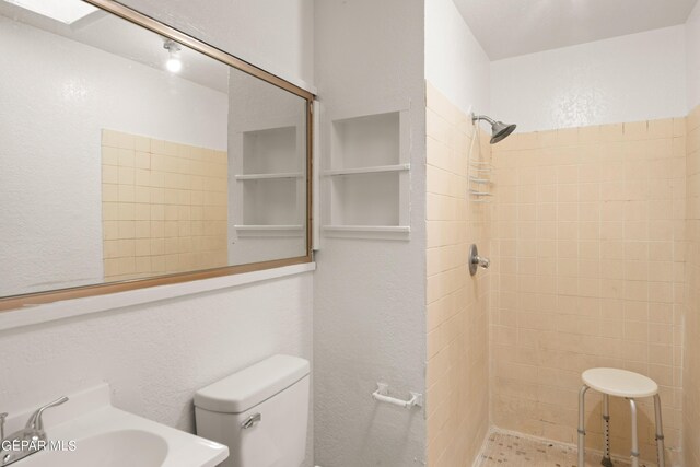 bathroom with toilet, tiled shower, and sink