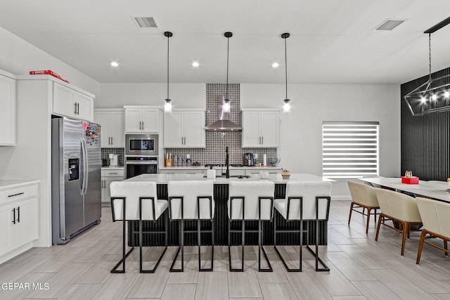 kitchen with an island with sink, pendant lighting, stainless steel appliances, and light hardwood / wood-style flooring