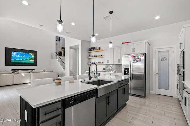 kitchen featuring hanging light fixtures, stainless steel appliances, white cabinetry, and a kitchen island with sink