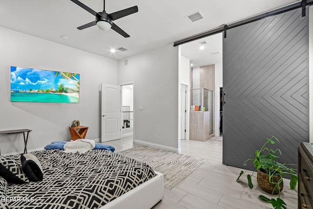 bedroom featuring light hardwood / wood-style flooring, ceiling fan, a barn door, and ensuite bathroom