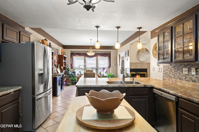 kitchen with a textured ceiling, stainless steel appliances, a tile fireplace, sink, and dark brown cabinetry