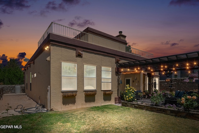 back house at dusk with a yard, a patio, and a balcony