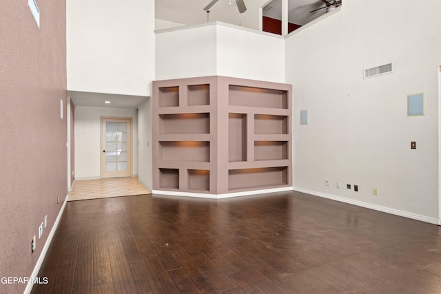 unfurnished living room featuring built in shelves, hardwood / wood-style floors, a high ceiling, and ceiling fan