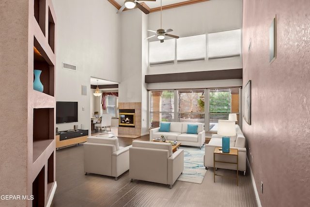 living room with a fireplace, ornamental molding, ceiling fan, a towering ceiling, and hardwood / wood-style flooring