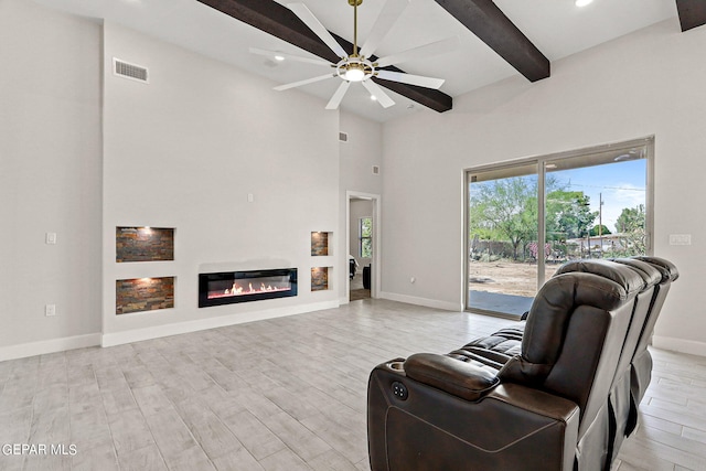 living room with a towering ceiling, beamed ceiling, light hardwood / wood-style flooring, and ceiling fan