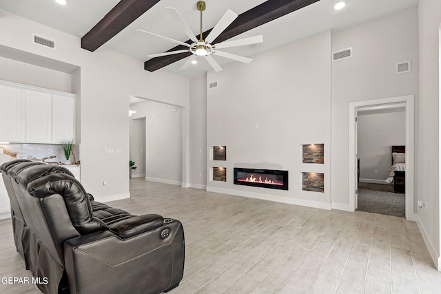 living room with light wood-type flooring, ceiling fan, beamed ceiling, and a towering ceiling