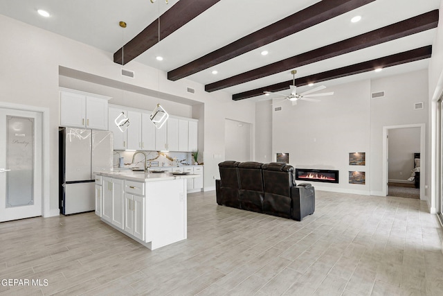 kitchen with light wood-type flooring, stainless steel fridge, white cabinetry, an island with sink, and ceiling fan