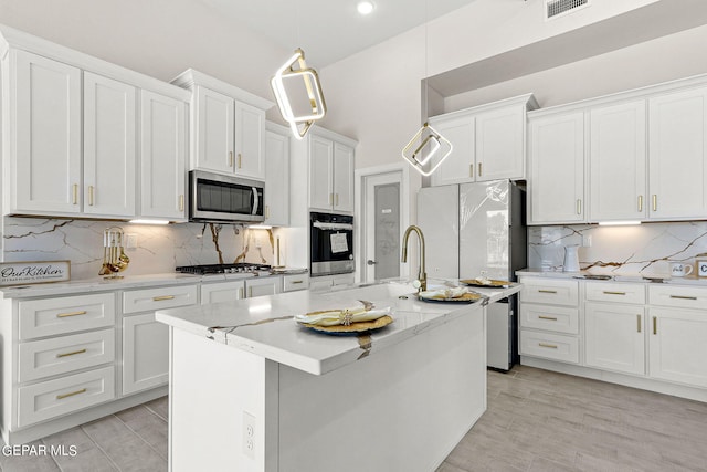 kitchen with decorative light fixtures, a center island with sink, stainless steel appliances, white cabinetry, and light wood-type flooring