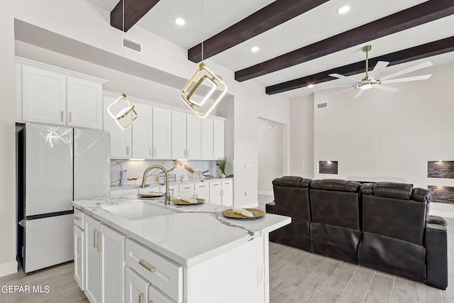 kitchen with light stone countertops, refrigerator, white cabinetry, ceiling fan, and a kitchen island with sink