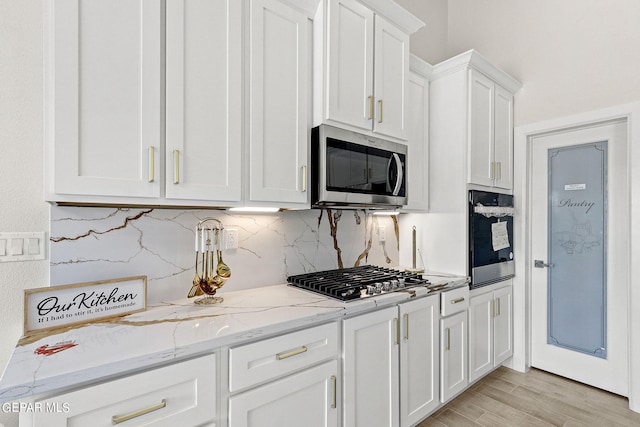 kitchen with light stone countertops, light hardwood / wood-style flooring, stainless steel appliances, and white cabinets