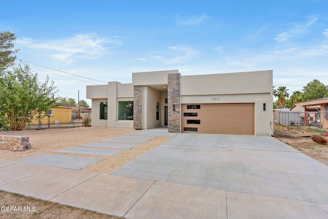 modern home with concrete driveway, fence, a garage, and stucco siding