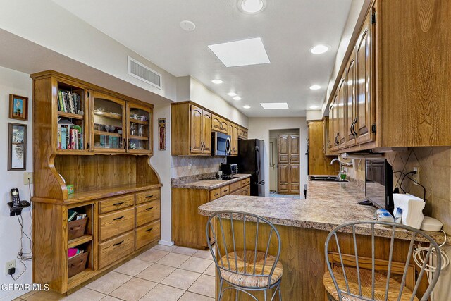 kitchen with a skylight, sink, black appliances, kitchen peninsula, and light tile patterned flooring