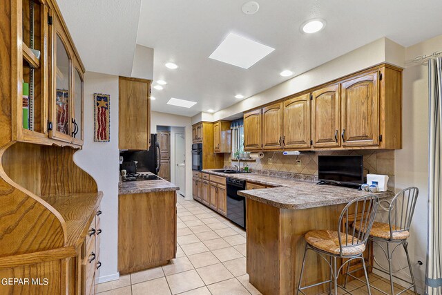 kitchen with tasteful backsplash, a skylight, a kitchen breakfast bar, black appliances, and kitchen peninsula