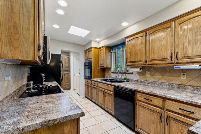 kitchen featuring black appliances, sink, tasteful backsplash, and a skylight