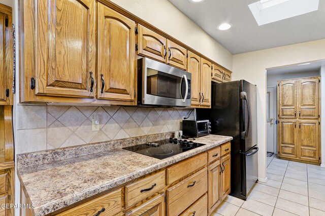 kitchen with black appliances, light tile patterned flooring, tasteful backsplash, and a skylight