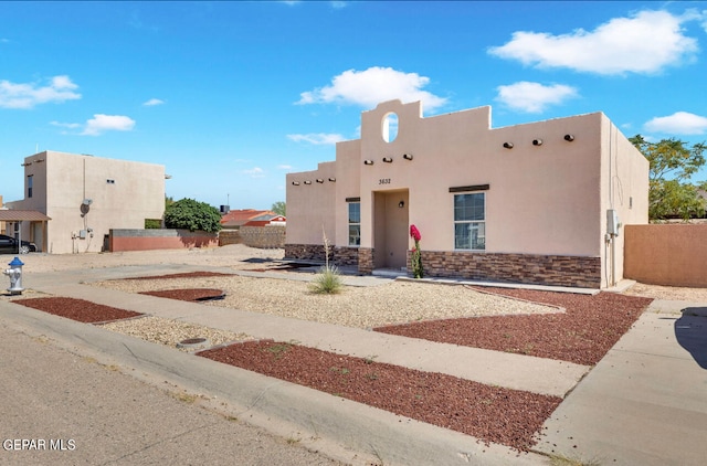 pueblo-style house featuring stone siding, fence, and stucco siding