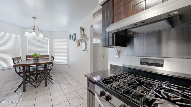 kitchen featuring stainless steel range with gas stovetop, light tile patterned floors, extractor fan, a chandelier, and dark stone countertops