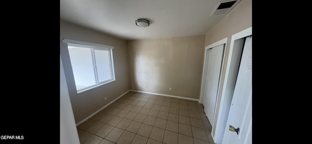 unfurnished bedroom featuring light tile patterned floors and multiple closets