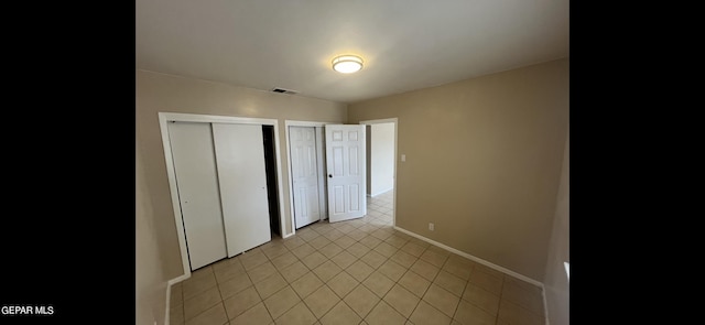 unfurnished bedroom featuring multiple closets and light tile patterned floors