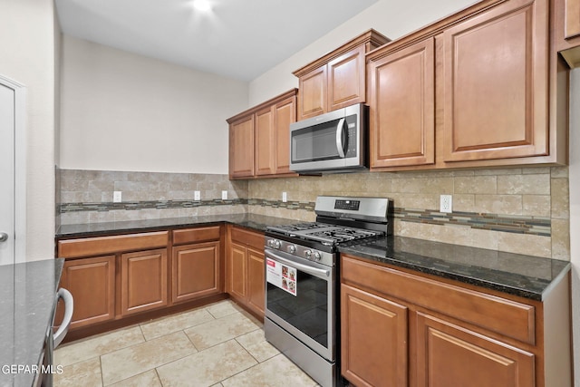 kitchen with dark stone countertops, light tile patterned floors, tasteful backsplash, and stainless steel appliances