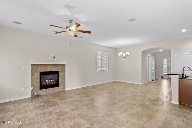 unfurnished living room with visible vents, a fireplace, arched walkways, a sink, and ceiling fan with notable chandelier