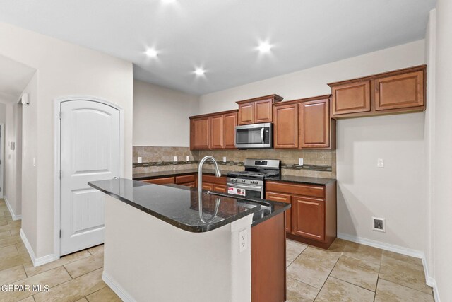 kitchen featuring a kitchen island with sink, dark stone countertops, stainless steel appliances, and decorative backsplash