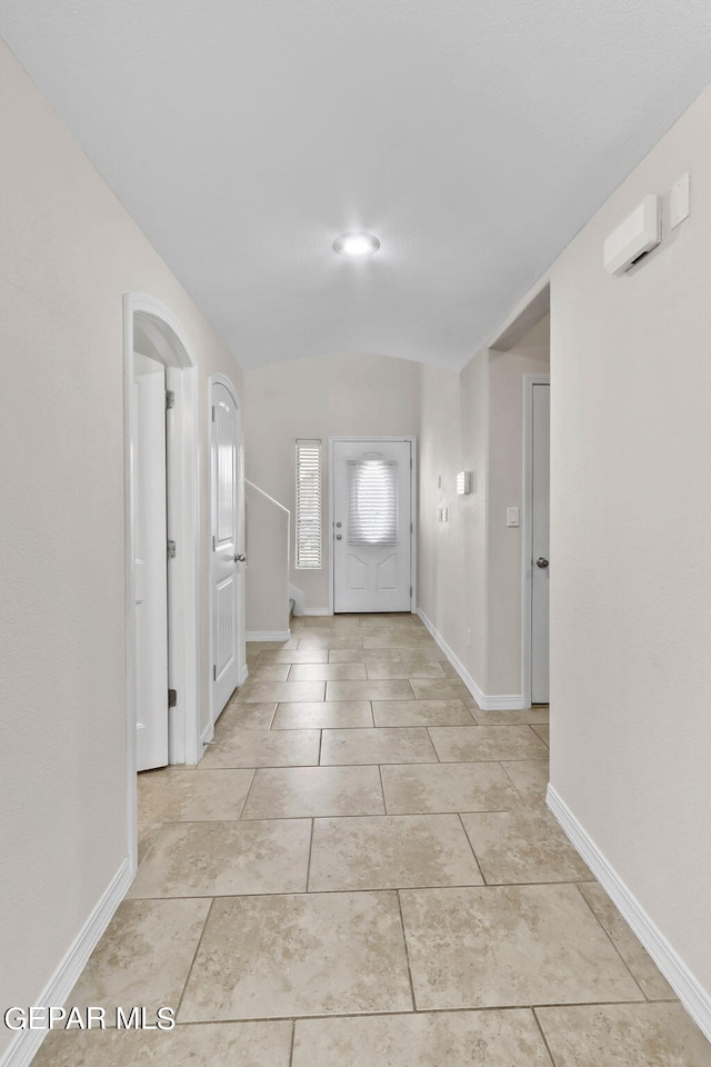 foyer entrance with light tile patterned floors, baseboards, arched walkways, and vaulted ceiling