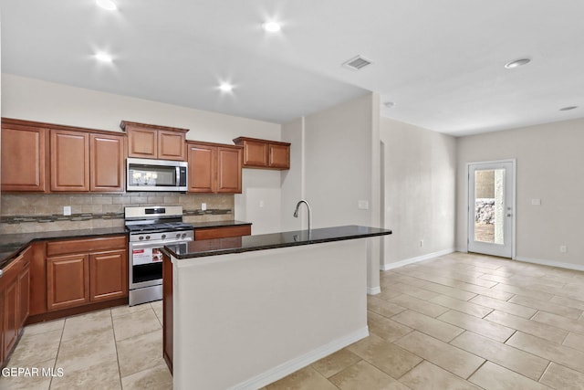 kitchen featuring dark stone countertops, appliances with stainless steel finishes, a kitchen island with sink, sink, and tasteful backsplash