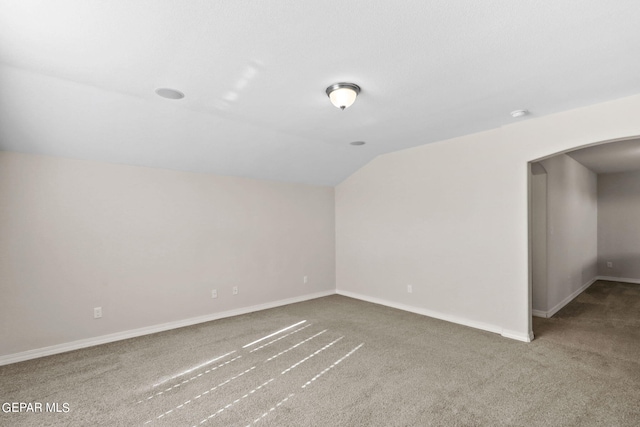 carpeted empty room featuring lofted ceiling, baseboards, and arched walkways