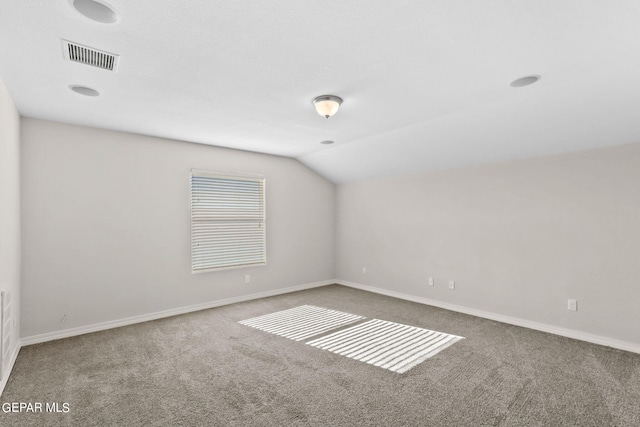 carpeted empty room featuring vaulted ceiling, baseboards, and visible vents