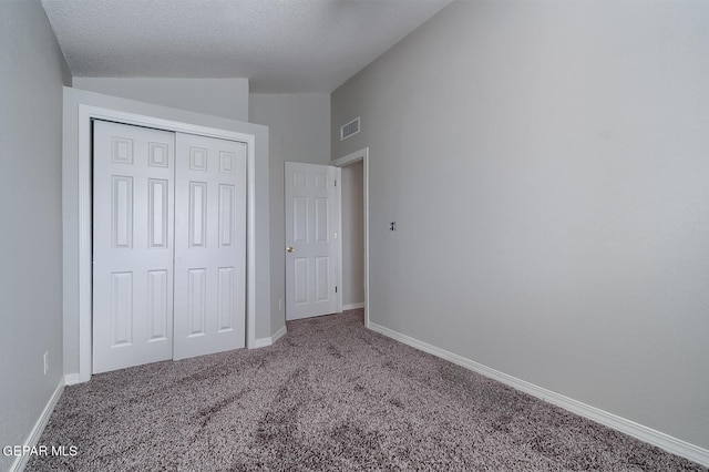 unfurnished bedroom with lofted ceiling, a textured ceiling, carpet floors, and a closet