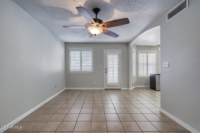 tiled empty room with a wealth of natural light, ceiling fan, and a textured ceiling