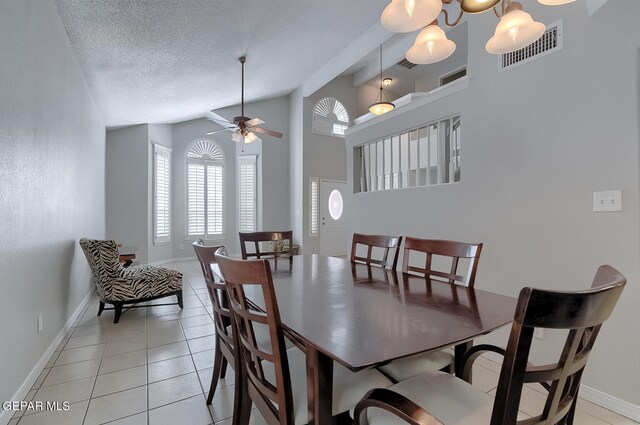 dining space with ceiling fan with notable chandelier, vaulted ceiling, a textured ceiling, and light tile patterned floors