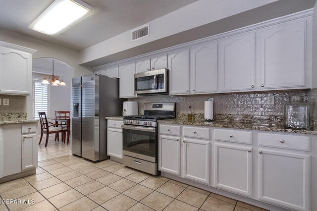 kitchen featuring dark stone counters, light tile patterned floors, an inviting chandelier, appliances with stainless steel finishes, and white cabinets