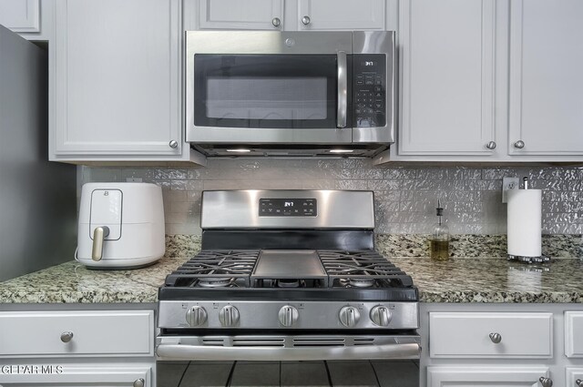 kitchen with white cabinets, backsplash, stainless steel appliances, and stone countertops