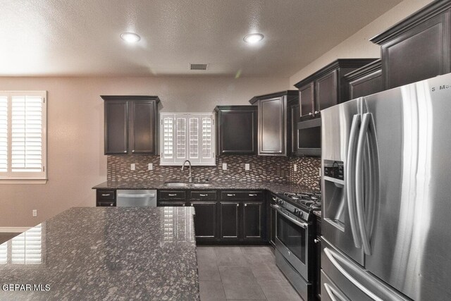 kitchen featuring dark stone countertops, dark tile patterned flooring, tasteful backsplash, sink, and appliances with stainless steel finishes