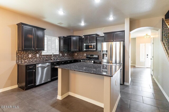 kitchen featuring dark tile patterned flooring, a center island, stainless steel appliances, decorative backsplash, and dark stone counters