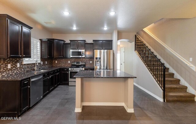 kitchen featuring a kitchen island, dark tile patterned floors, stainless steel appliances, sink, and dark stone countertops