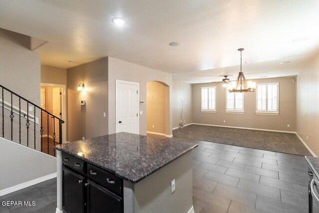 kitchen featuring dark stone countertops, a textured ceiling, decorative light fixtures, a kitchen island, and an inviting chandelier