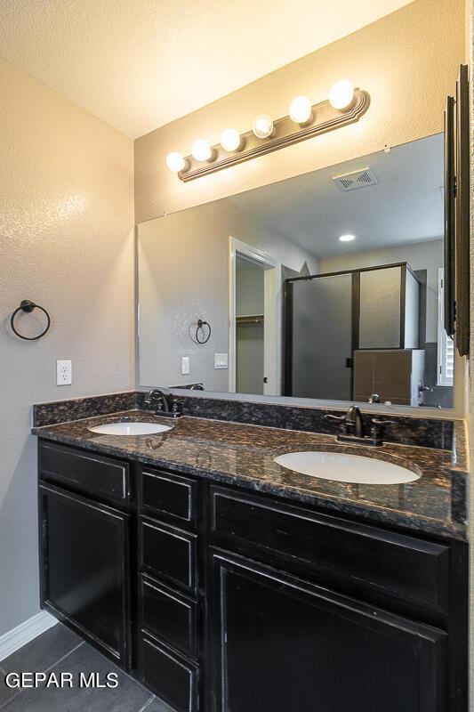 bathroom featuring a shower with shower door, vanity, a textured ceiling, and tile patterned floors