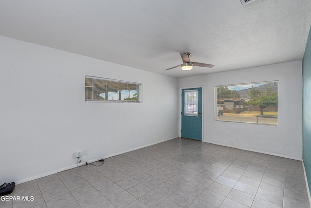 spare room with a textured ceiling, light tile patterned floors, and ceiling fan