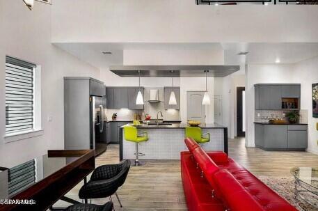 kitchen with gray cabinetry, light wood-type flooring, wall chimney range hood, stainless steel fridge, and decorative backsplash