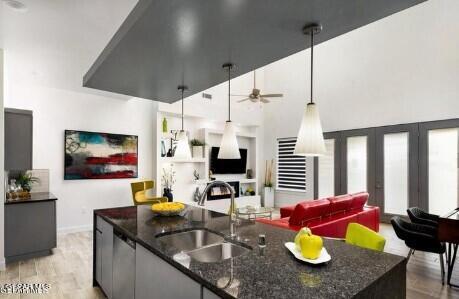 kitchen with light hardwood / wood-style flooring, dark stone countertops, sink, and hanging light fixtures