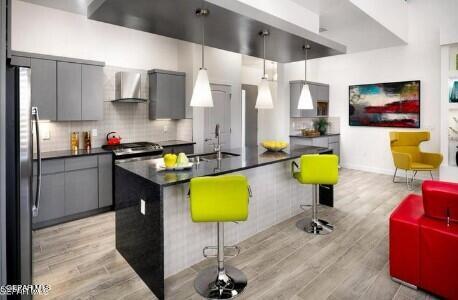 kitchen with hanging light fixtures, light hardwood / wood-style flooring, appliances with stainless steel finishes, wall chimney range hood, and a kitchen breakfast bar