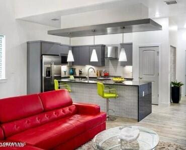 interior space featuring wall chimney exhaust hood, stainless steel refrigerator with ice dispenser, pendant lighting, light hardwood / wood-style floors, and sink