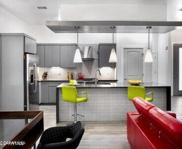 kitchen featuring backsplash, wall chimney range hood, sink, stainless steel refrigerator with ice dispenser, and light hardwood / wood-style floors