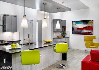 kitchen featuring hanging light fixtures, sink, decorative backsplash, and light hardwood / wood-style floors